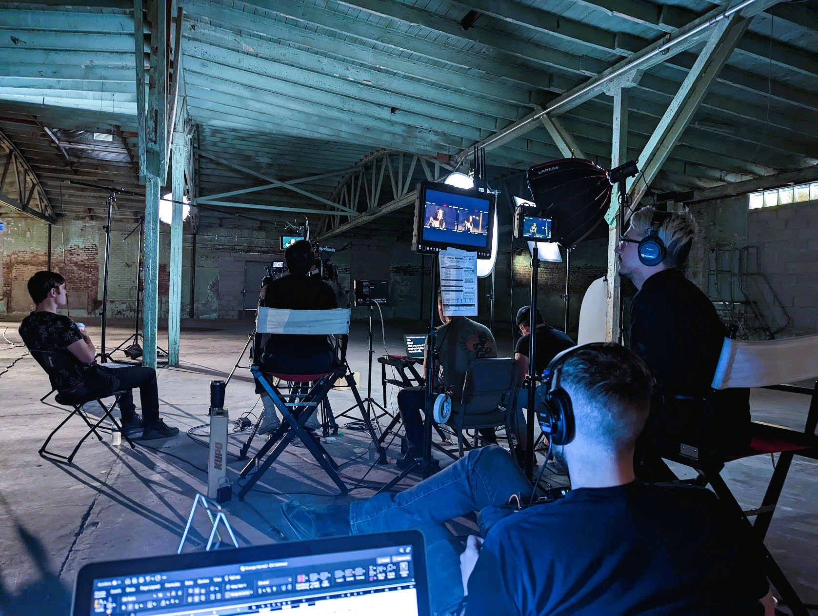 Behind the scenes photo of the film crew setting up an interview scene for the horror mockumentary Strange Harvest inside an industrial warehouse location.